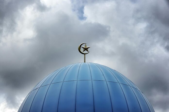 Blue mosque dome with crescent and star against a cloudy sky, showcasing modern Islamic architecture.